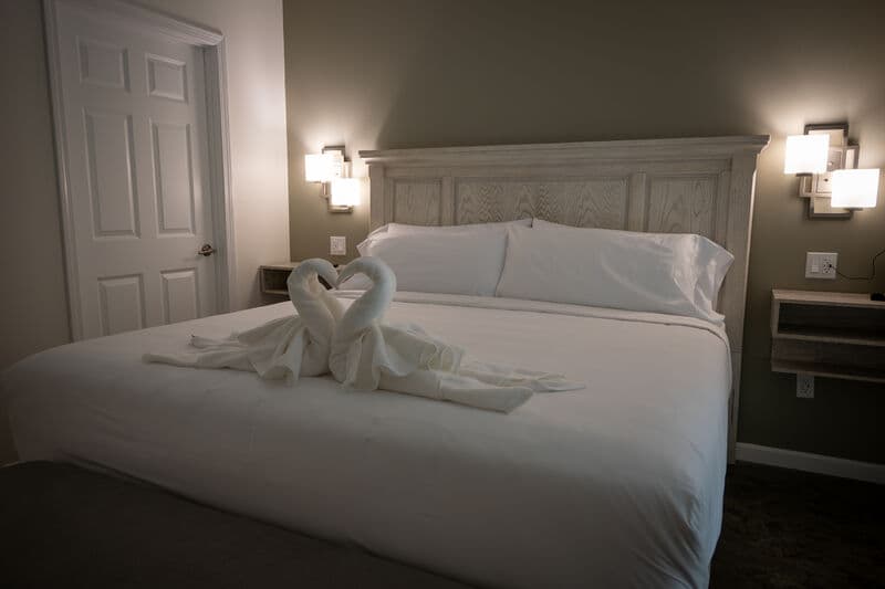 dimly lit bedroom, white linens with swan shaped white towls on end of bed.
