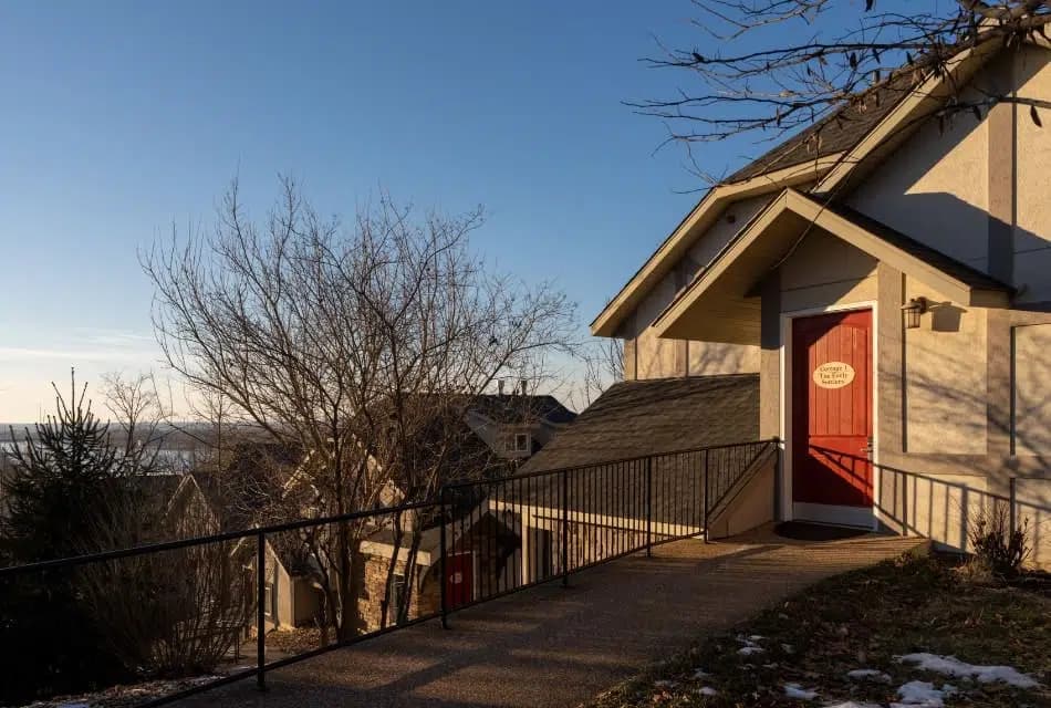 Exterior view of one of the cottages with pathway leading up to red door surrounded by trees and sun shining in the background