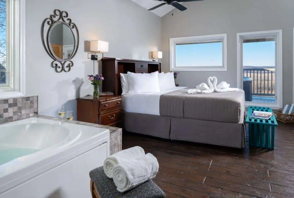 Large bedroom suite with light gray walls, tiled flooring, wooden headboard, white bedding, gray comforter, and jetted tub