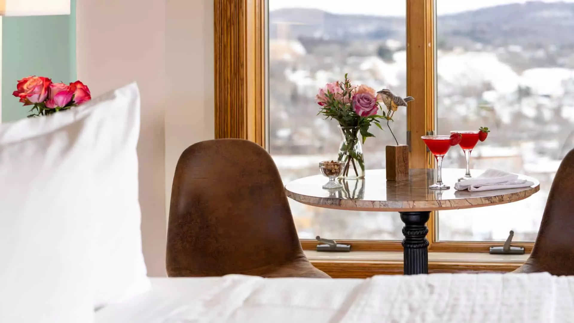 Close up view of a bedroom sitting area with brown armless chairs and small table with cocktails and vase with flowers on top