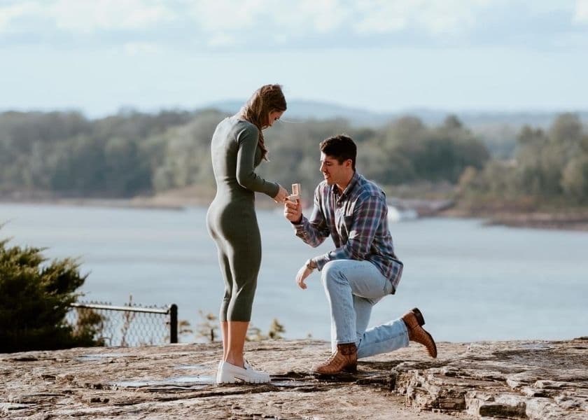 man proposing marriage to woman with open ring box while kneeling on the missouri river bluff man proposing marriage to woman with open ring box while kneeling on the missouri river bluff