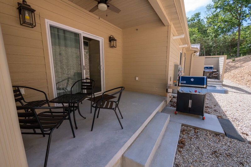 Grill and outdoor table and chairs on concrete patio with sliding glass doors into condo behind the table.