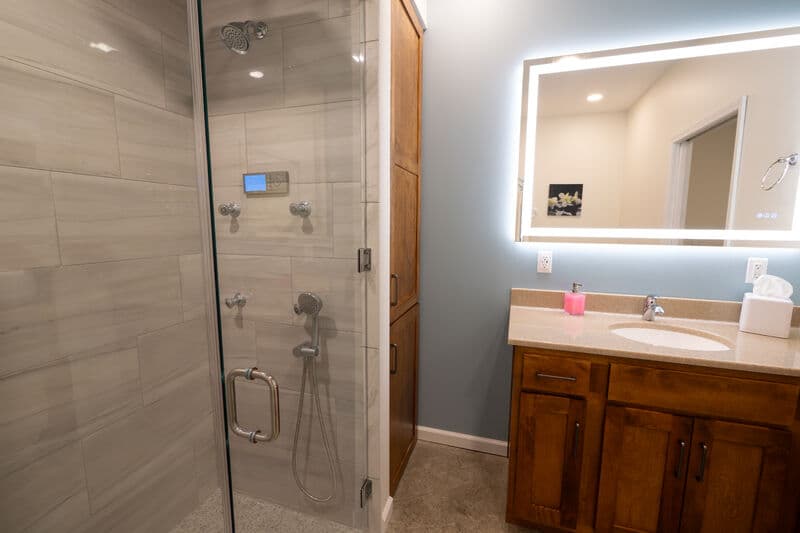 walk in shower and vanity with sink. large mirror above sink has a led light frame all the way around it.