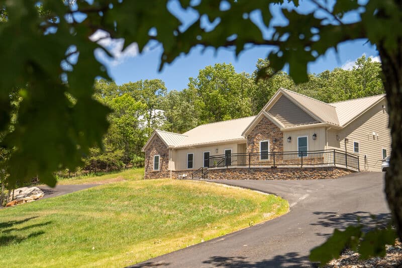 exterior photo taken from under a tree of single story building and driveway. building has ramp to main entrance.