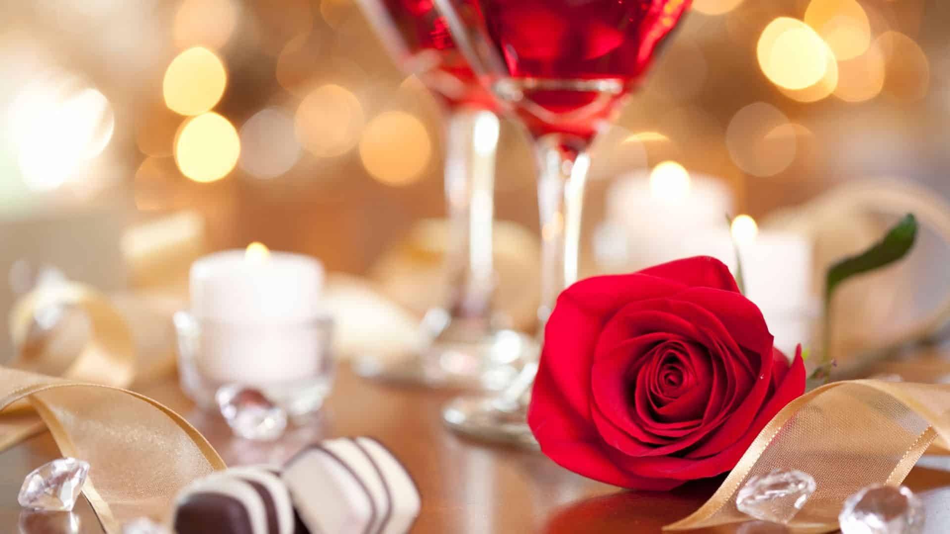 Red rose, two red wine glasses, candles, diamonds and twinkle lights