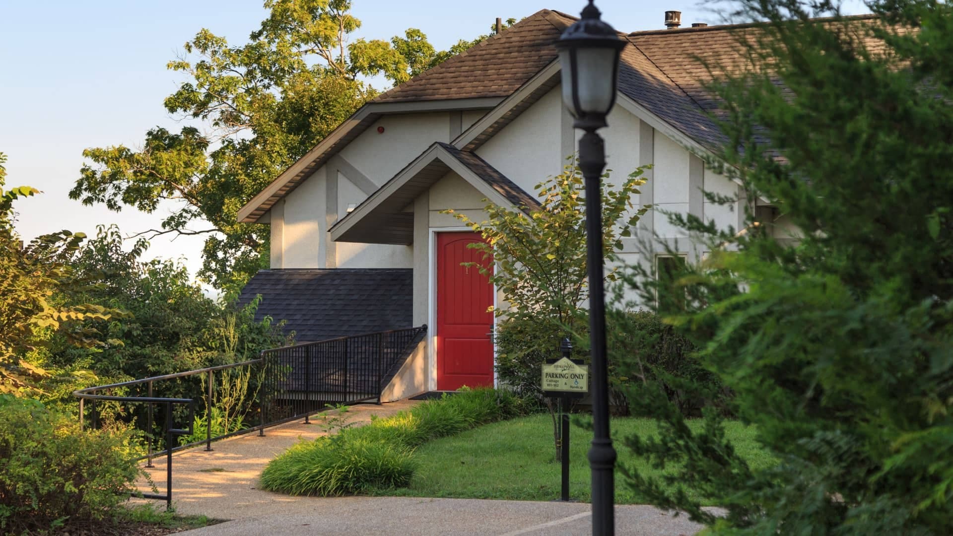 Exterior view of one of the cottages with pathway leading up to red door surrounded by trees and other green vegetation