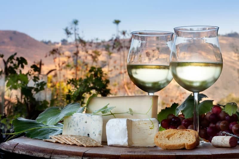 a plate of fancy cheese and crackers and two glasses of white wine