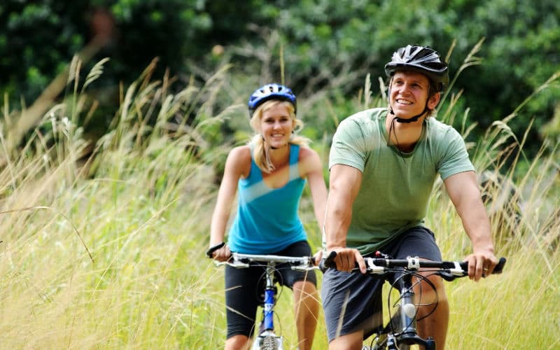 a couple riding bicycles near a field