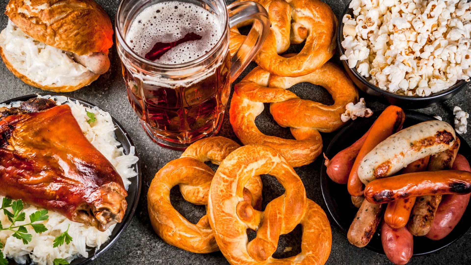 An array of German food, like popcorn, brats, sausage, pretzels, beer, and chicken