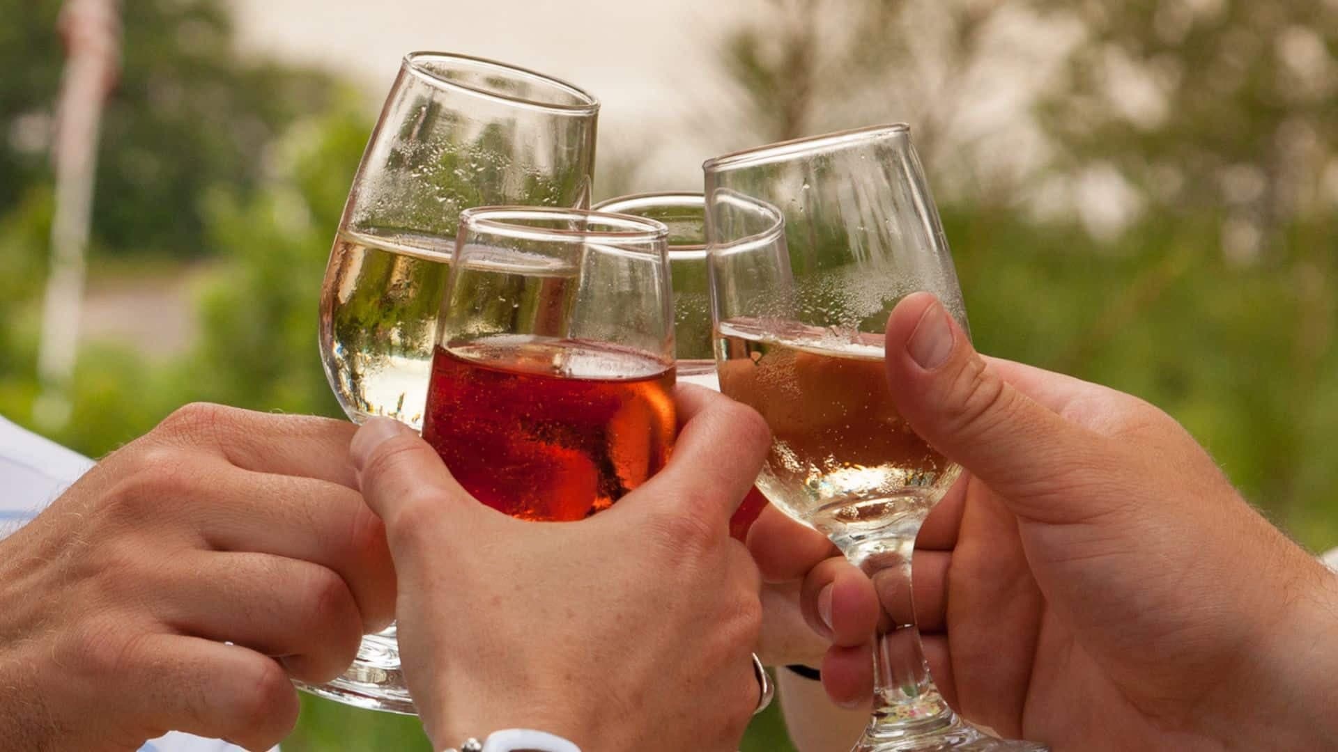 Four hands clinking wine glasses filled with red wine with trees in the background