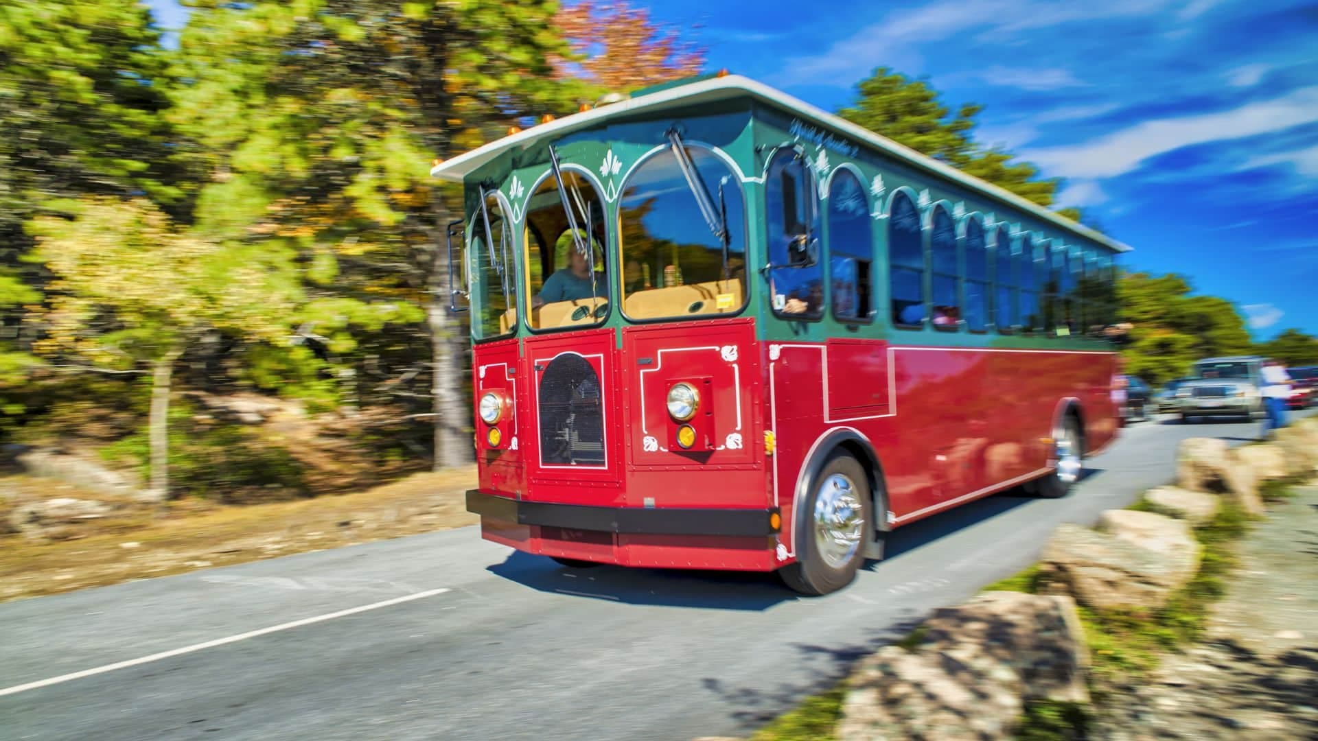 red and green trolley on a street speeding by trees with surrounding scene blurred