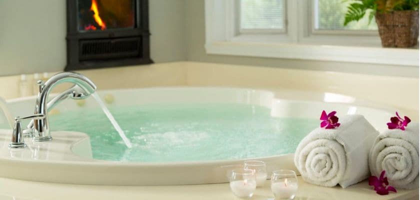 two rolled towels with pink flowers next to a trio of candles by a jetted tub