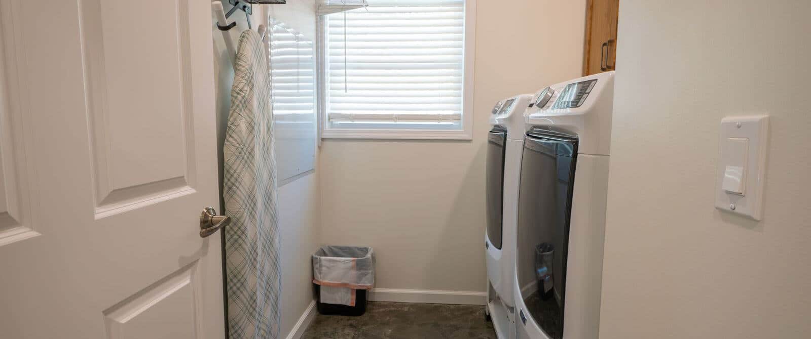 Well-lit laundry room with side-by-side appliances with ironing board handing on wall.