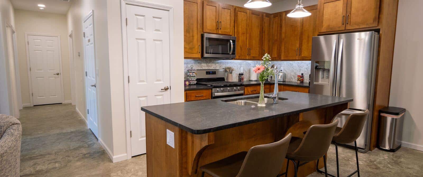 View of kitchen with center island with cushioned brown chairs, stainless steel appliances, lots of cabinets, hallway to other rooms