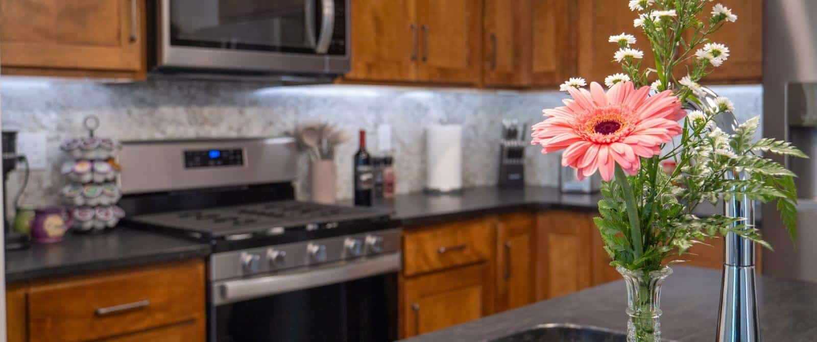 Closeup view of counter with stainless steel range and microwave hanging above, lots of cabinets, keurig coffee pods next to machine, center island